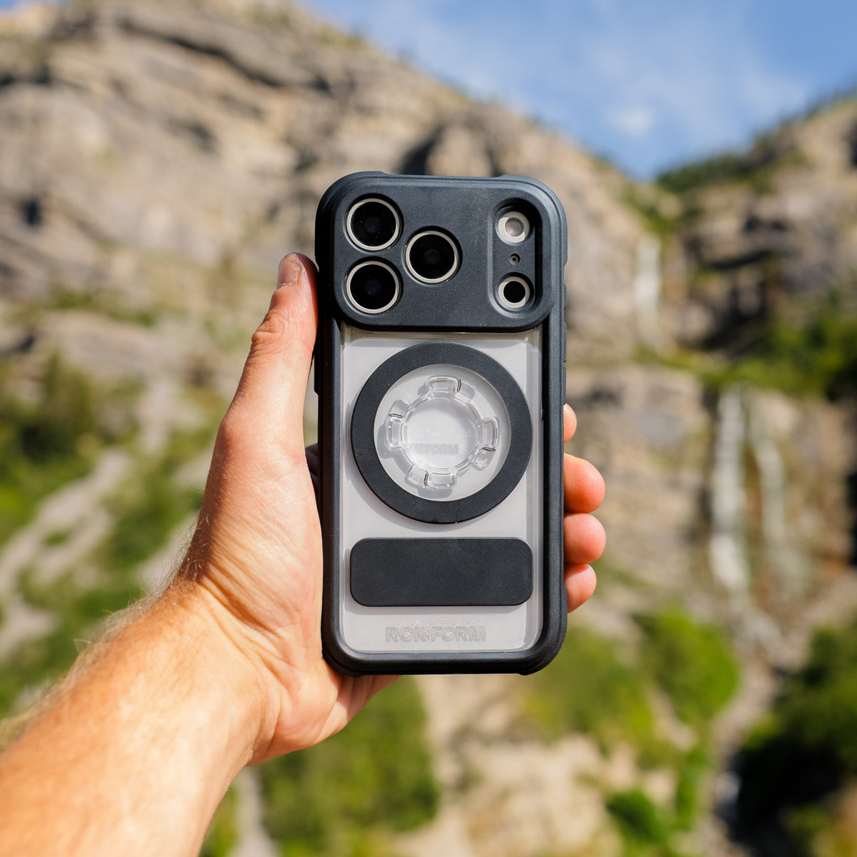 Hand holding a Rokform Crystal Case against a mountain landscape
